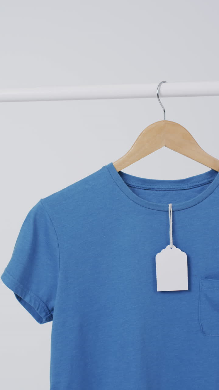 Vertical video of blue t shirt with tag on hanger and copy space on white background