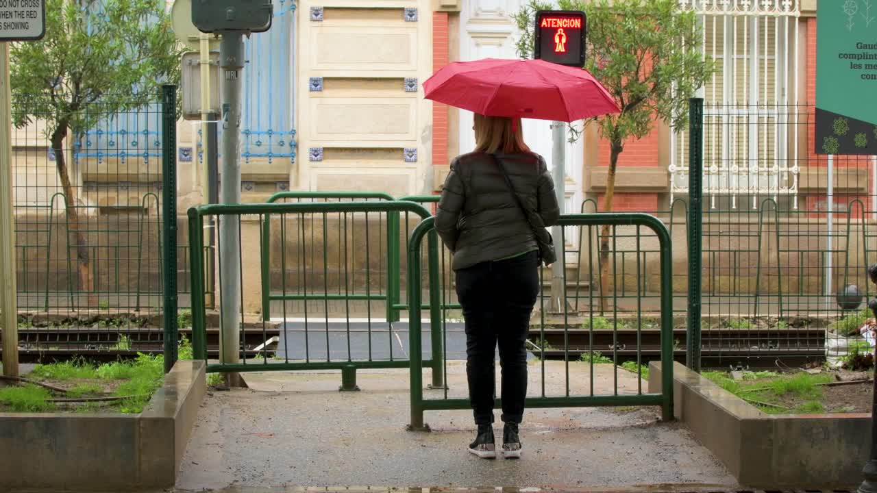 Girl with umbrella waiting for the train to pass while flashing a level crossing sign. Spain.
