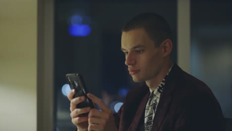 Young-Adult-Professional-Caucasian-Guy-Sitting-Inside-The-Office-Holding-His-Smartphone-Browsing---Medium-Shot