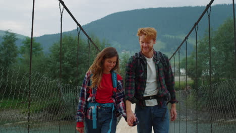 hitchhikers walk mountains together on river bridge. couple hold hands outside.