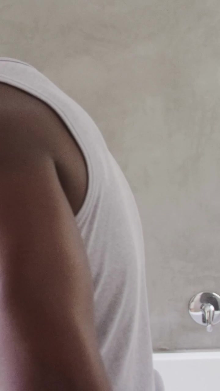 Vertical video: Appearing left, man in tank top leaning to turn tap on bathroom tub rim with tray