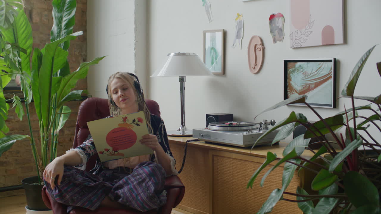 Mujer escuchando música y leyendo la carátula de un disco de vinilo junto al tocadiscos.