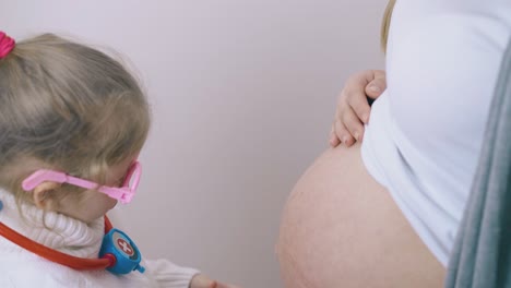 una niña pone un estetoscopio de juguete en el vientre de su madre embarazada en casa