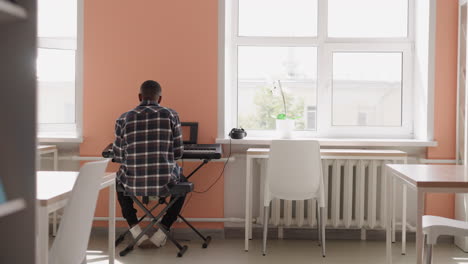 hombre negro se involucra con sintetizador. artista afroamericano ensaya melodía en instrumento eléctrico en la academia de música. preparación para la actuación