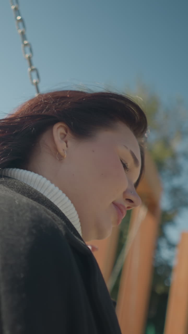 야외에서 흔들리는 여자의 클로즈업, 그녀의 머리카락이 부드럽게 바람에 흔들리고, 사슬을 들고, 흐릿한 사람들과 울창한 초록색으로 은 공원을 배경으로 설정