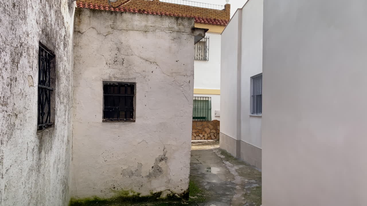 Vicolo urbano che presenta un contrasto architettonico tra vecchi muri logori ed edifici moderni con grate di sicurezza.
