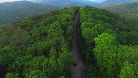 Drone-footage-of-car-with-canoe-driving-up-NH-White-Mountains-through-forest-on-dirt-road