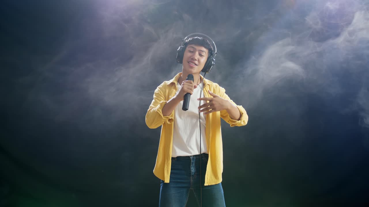 헤드폰을 들고 마이크를 들고 색 연기가 검은색 배경에 하는 아시아 소년