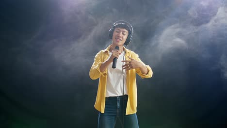 헤드폰을 들고 마이크를 들고 색 연기가 검은색 배경에 하는 아시아 소년