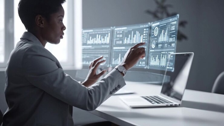 Professional woman engaged in analyzing data on a futuristic holographic interface while sitting at a modern workspace with a laptop and a focused expression.