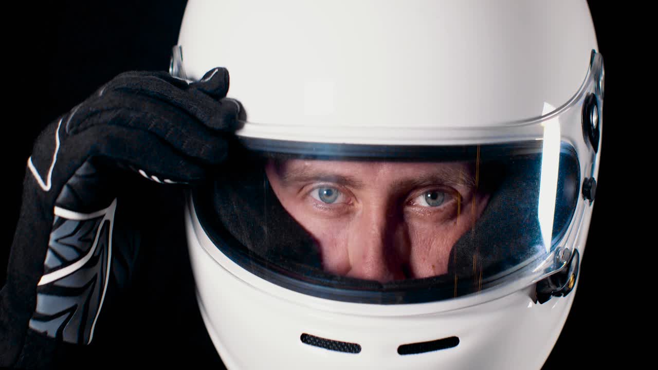 Mann med sterke blå øyne som ser inn i kameraet og lukker hjelmvisiret i 4K sakte film.