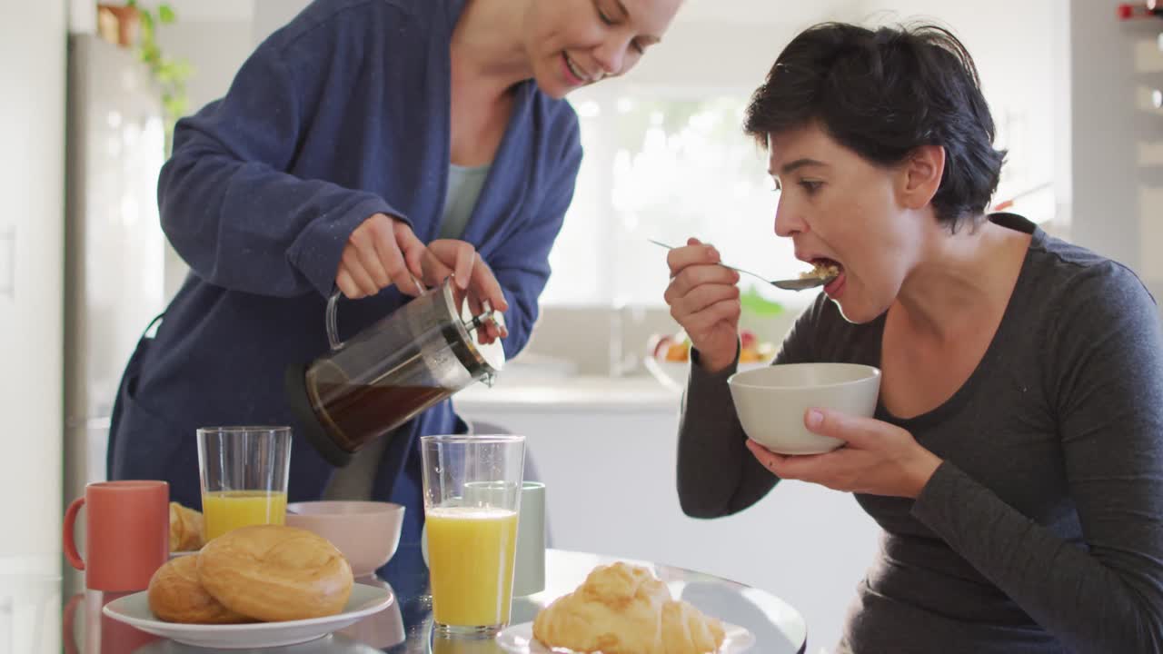 백인 여성 이 집 에서 아내 와 함께 아침 식사를 하는 동안 컵 에 커피 를  ⁇ 고 있다