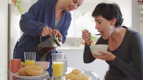 caucasian woman pouring coffee in a cup while having breakfast with her wife at home