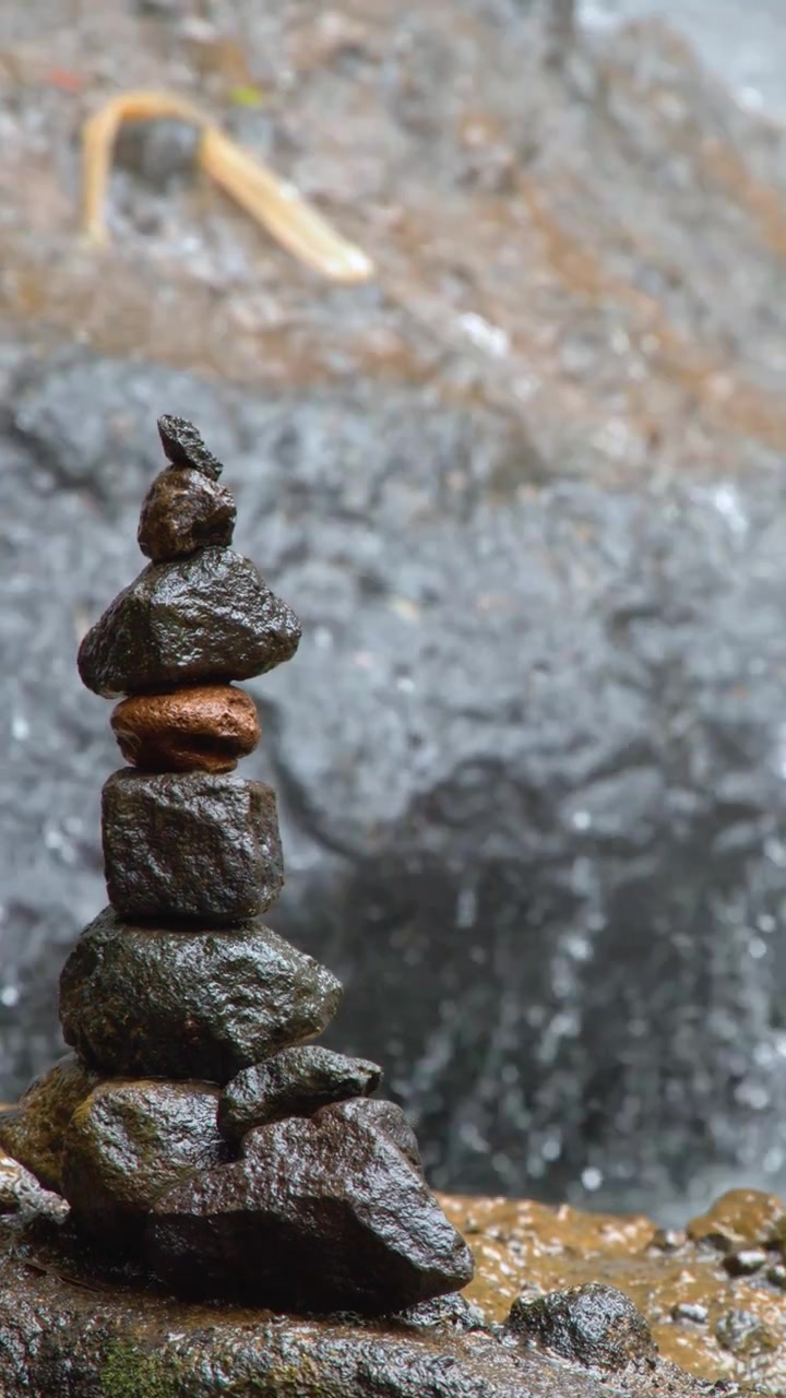 Una pila di pietre in equilibrio si trova su massi bagnati davanti a una cascata tropicale impetuosa