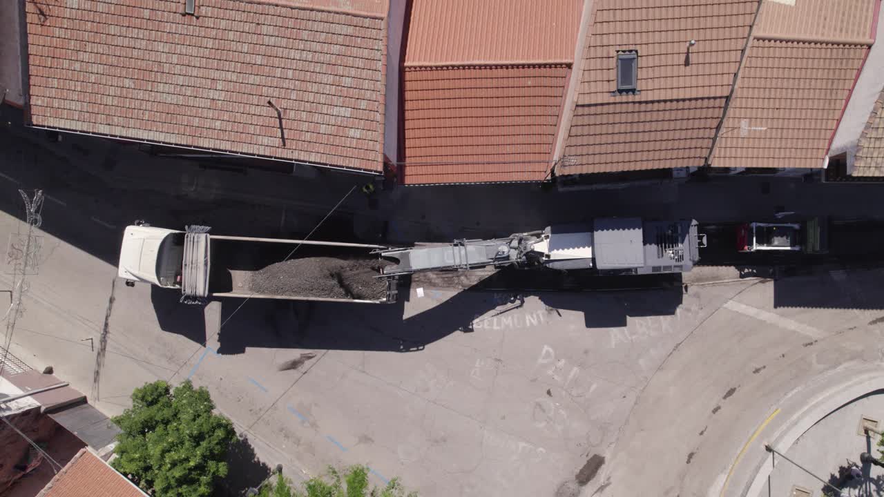 Vista aerea a volo d'uccello su un veicolo per lavori stradali che carica asfalto su un camion per il ripristino stradale a Navas del Rey, Spagna