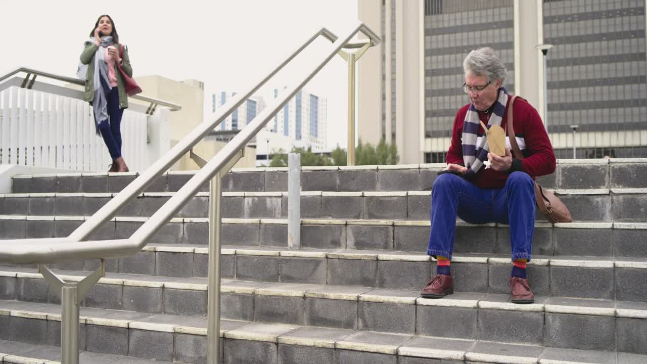 White man eating from box checking phone on steps as Hispanic woman descending stairs calling
