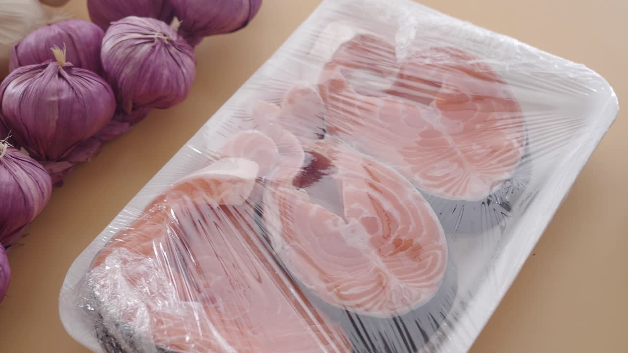 Raw Salmon Fillet in Packaging with Purple Onions and Garlic