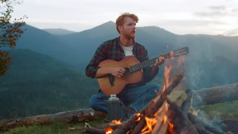 el viajero pensativo toca la guitarra al aire libre. el tipo se sienta junto a la montaña, la naturaleza, la fogata.