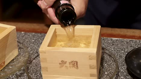 pouring sake into square wooden cup