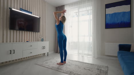 mujer joven meditando sentada en la alfombra y haciendo splits estirándose haciendo yoga ropa deportiva azul habitación luminosa en casa por la mañana. mujer practicando yoga en casa