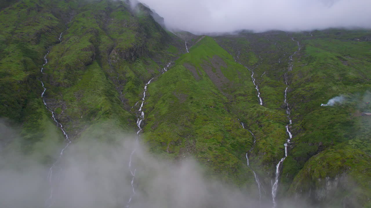 4K luftfoto af vildt landskab med vandfald dækket af skyer og himmelske grønne bakker i Nepal