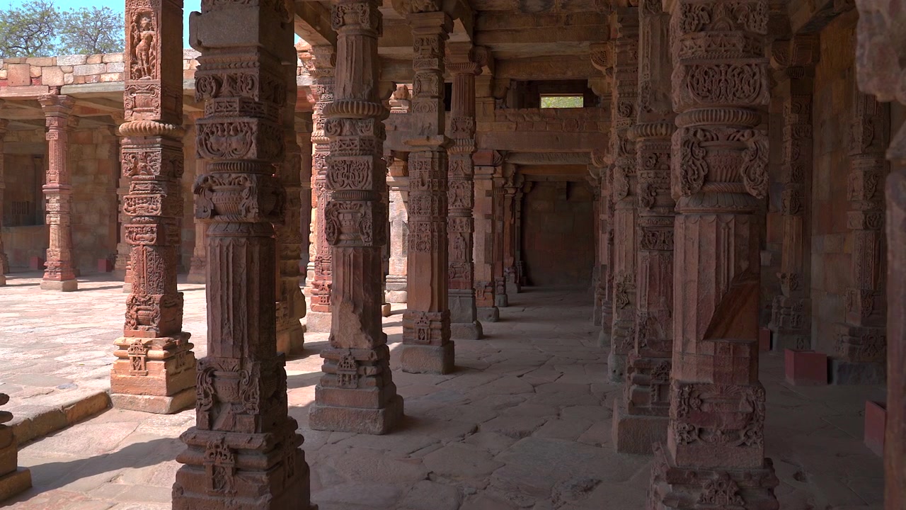 Inquadratura ampia statica degli storici pilastri in arenaria finemente intagliati all'interno del chiostro della moschea Quwwat-ul-Islam nel complesso di Qutb a Nuova Delhi, India