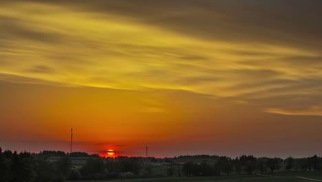 picturesque landscape with orange colored sunset behind forest trees and flying soft clouds at sky in the evening - time lapse panorama view