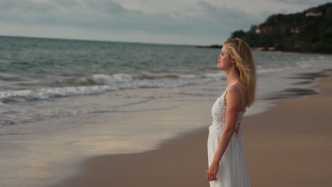 Chica-Rubia-Relajándose-En-La-Playa-Con-Un-Lindo-Vestido-Blanco,-Sonriendo-A-La-Cámara