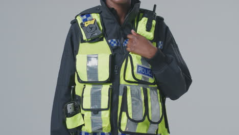 full length studio portrait of smiling young female police officer against plain background