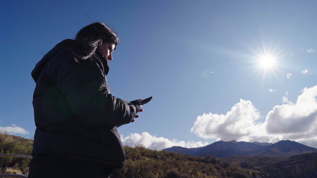 Female traveler raises her phone to capture signal in remote desert setting, symbolizing intersection of technology, connectivity, and outdoor exploration