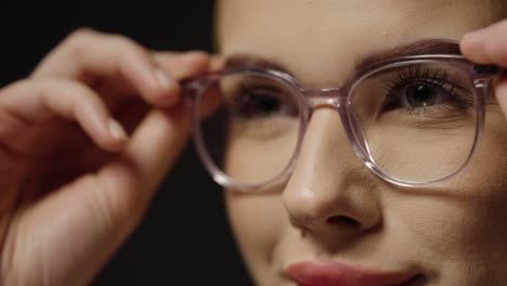 Close-up-of-a-young-pretty-woman-putting-on-glasses-as-a-visual-aid-for-better-vision-to-see-more-clearly-with-better-eyesight-in-slow-motion-against-black-background