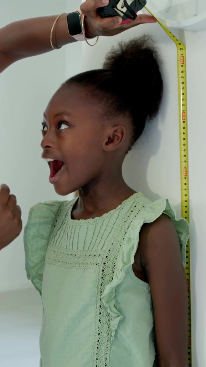 Vertical video: Placing yellow tape measure mother measuring child by wall in hall marking height