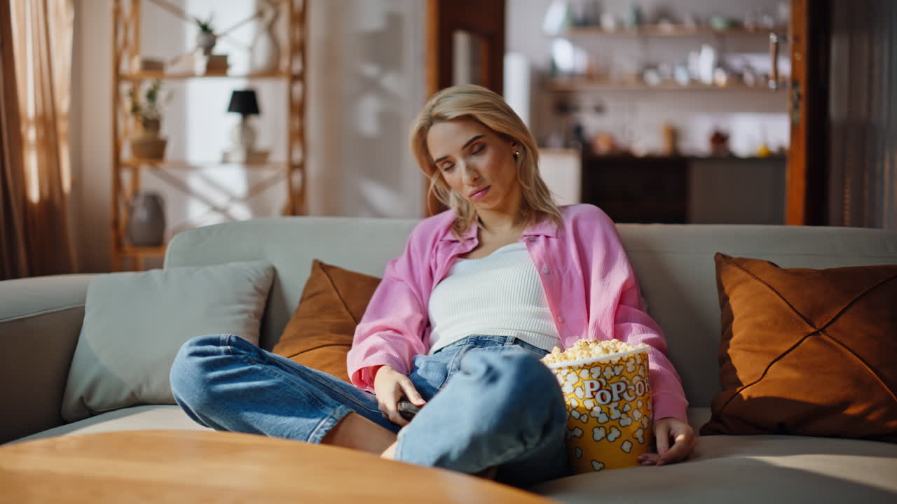 Blonde girl switching channels by remote controller. Happy lady enjoy serial