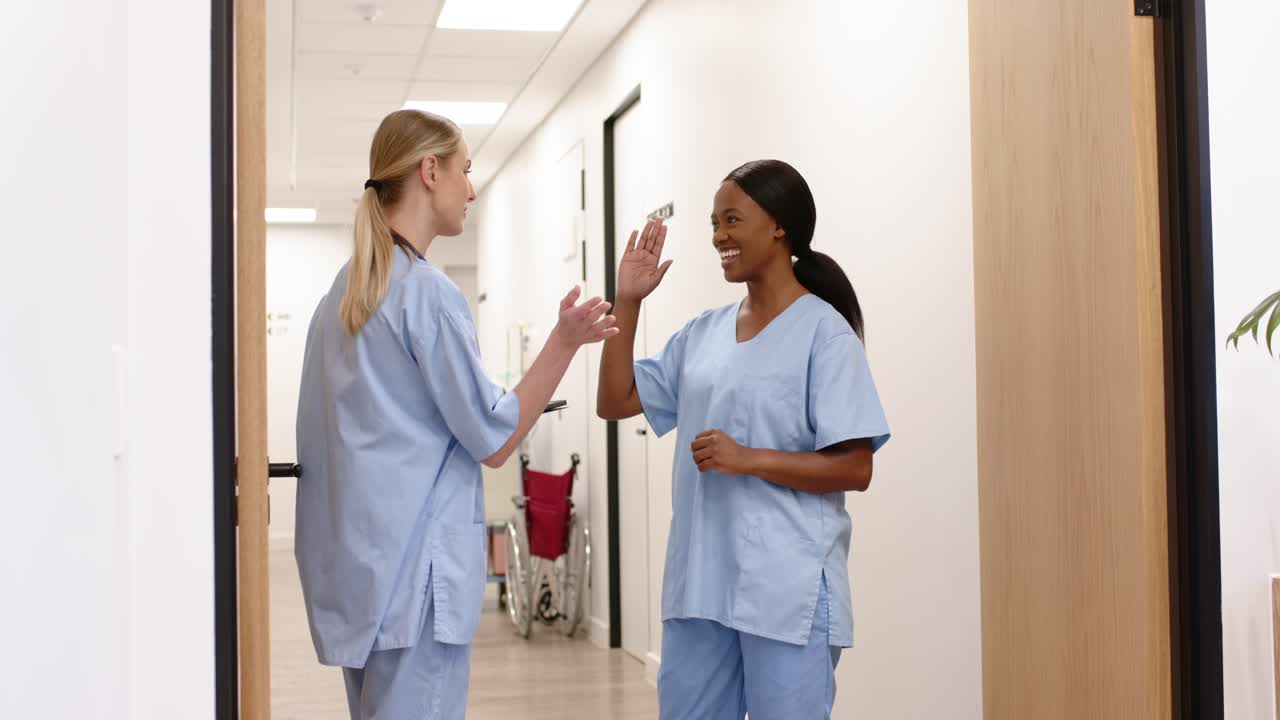 Two female nurses referencing tablet while walking and talking in clinic corridor, swapping badge
