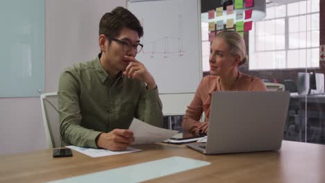 diverse male and female business colleagues in discussion in meeting room using laptop