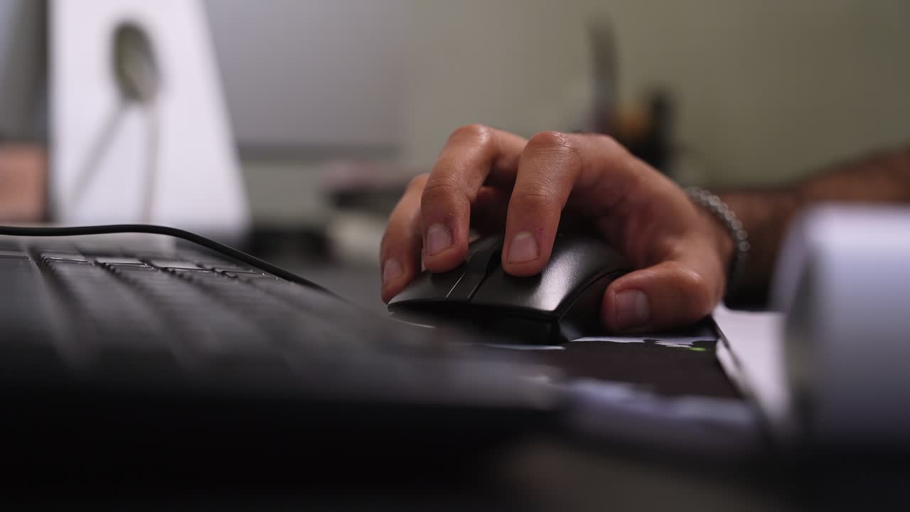 shot of a hand using a black computer mouse on a desk next to a keyboard. This indoor workspace scene highlights daily productivity and technology in a modern corporate office