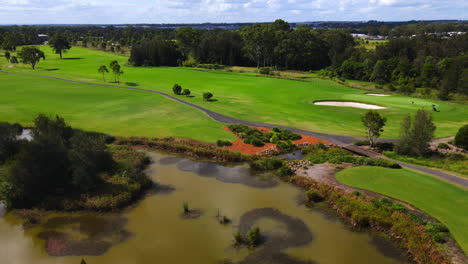 fast drone pan over golf course with golfers teeing beautiful blue sky pan to lake and suburban community