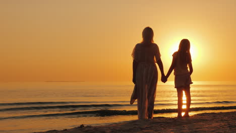 A-Woman-Holds-A-Child's-Hand-Stand-Together-On-The-Seashore-Look-At-A-Beautiful-Sunset-Mother-With-D