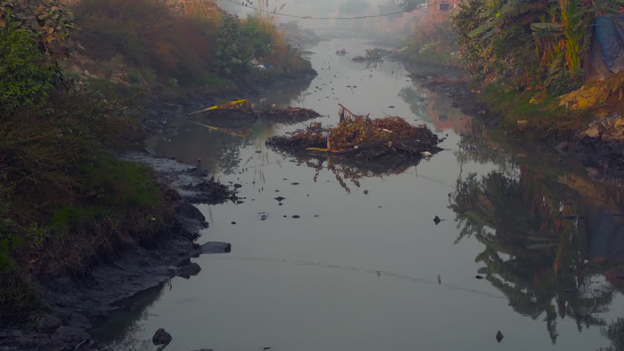 gran grifo de agua de alcantarillado en la sociedad, sahiwal pakistan, casas y árboles en el grifo, agua sucia, plantas y basura en el agua, cuervos volando sobre el grifo