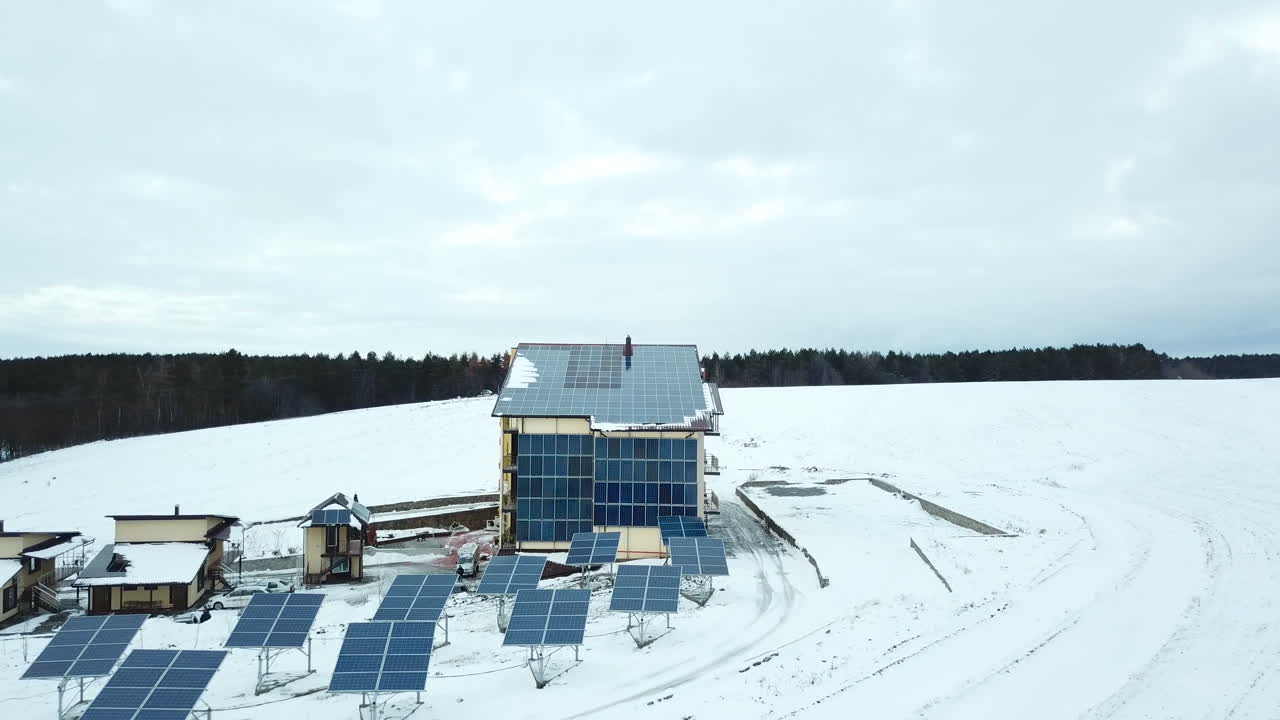 Hotel complex in the mountains with solar panels on the snow. Rows of snow covered solar panels in a small solar power plant.