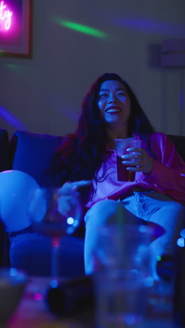 video vertical de una mujer borracha sentada en el sofá bebiendo alcohol en una fiesta en casa