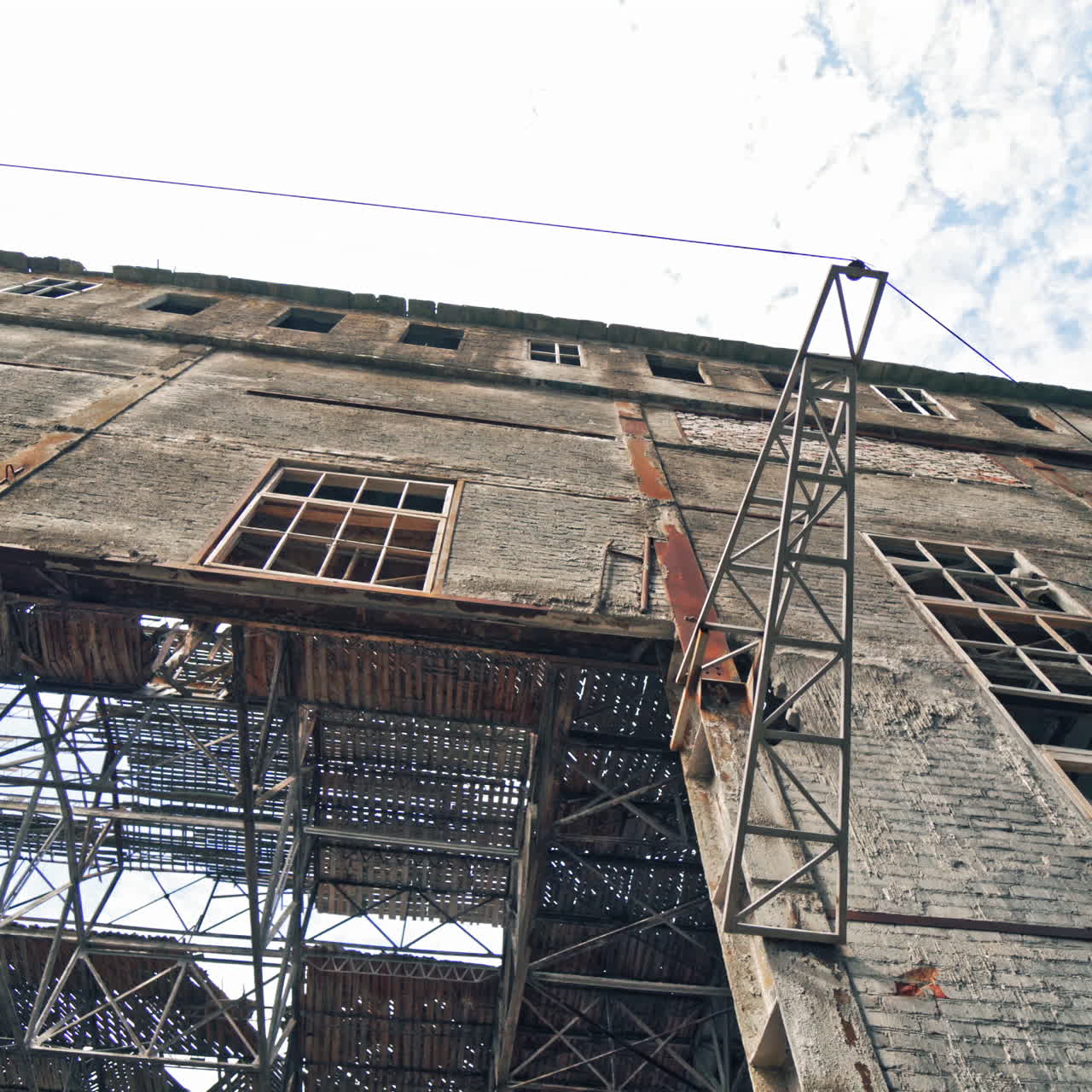 Old abandoned plant with broken windows ruined after the military actions. Demolished plant with pitted roof and some snow on the ground in winter. Bottom view