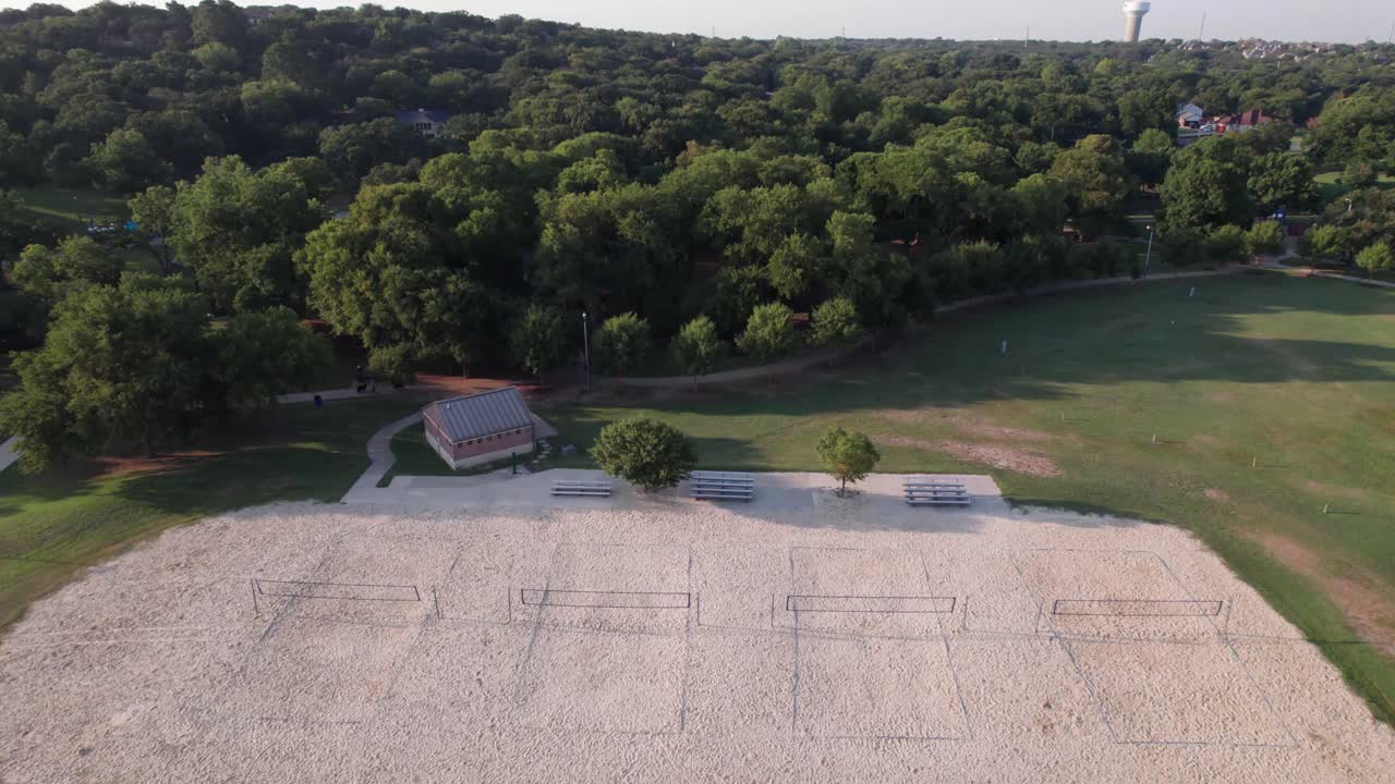 Aerial footage of sand volleyball court in Bear Creek Park in Keller, Texas. Camera slowly approaches and flies over the court