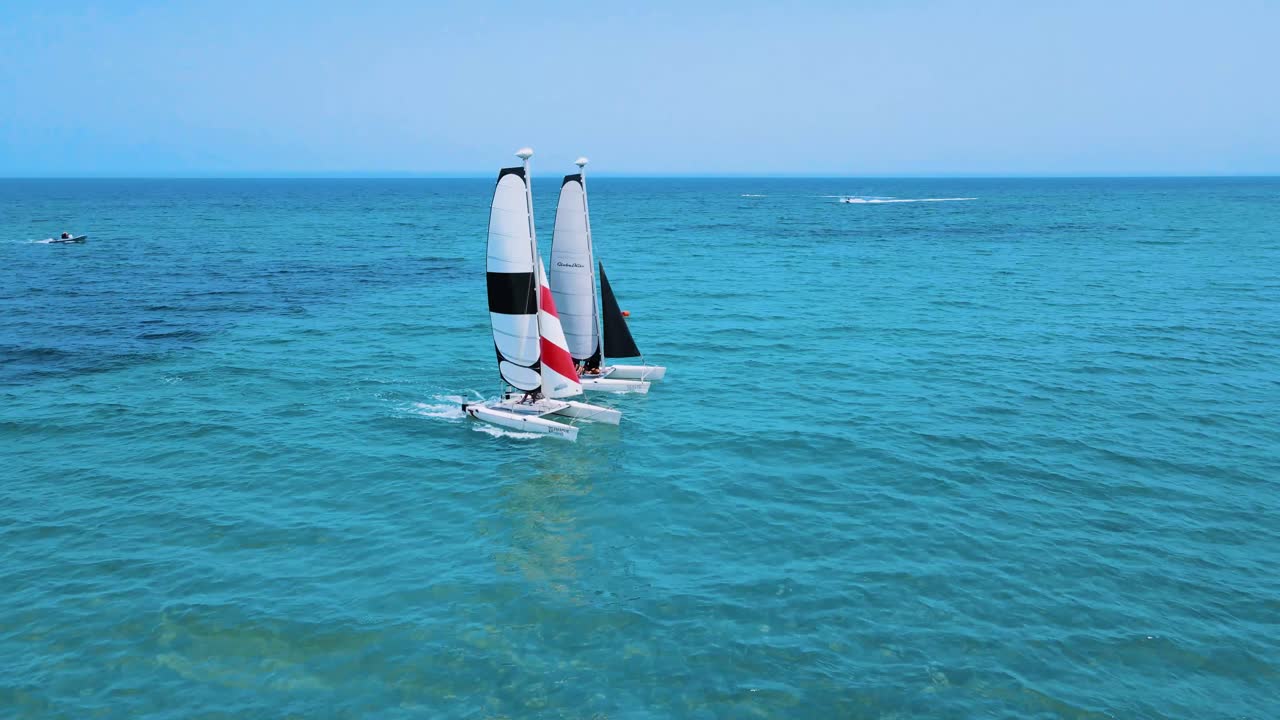 An aerial view of Two Catamaran sailboats are floating on the water, each with a person controlling it close together, and there is another boat further away in the background. at Tunisia Djerba