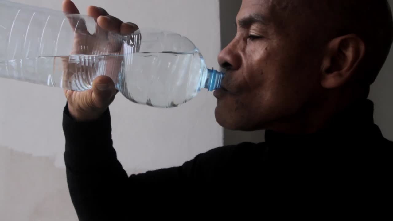 hombre bebiendo agua de una botella de plástico con fondo gris video de stock