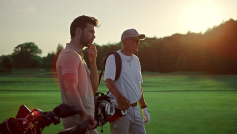 rich men playing golf on sunset summer course. two players enjoy sport on field.