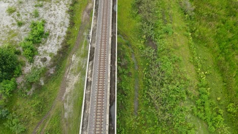 Aerial-reverse-footage-over-a-railway-revealing-a-wetland-below-and-some-pockets-of-water,-farmlands