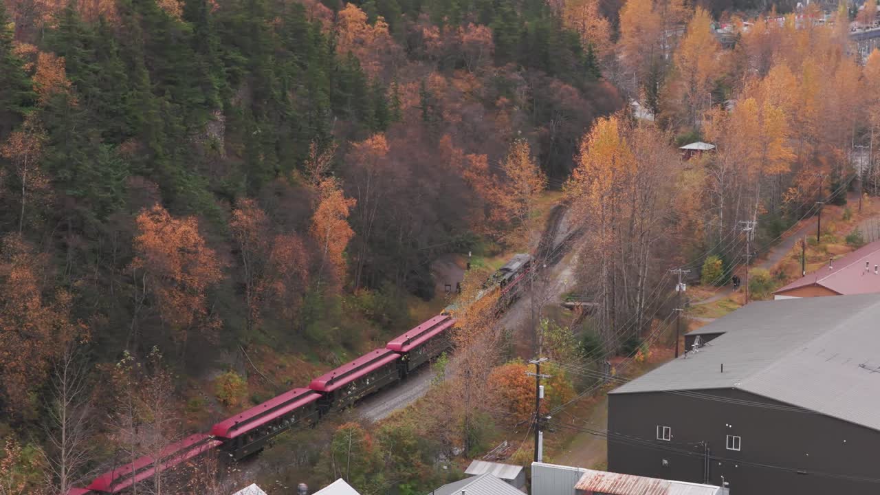 Telephoto aerial shot following the White Pass Yukon Route train as it approaches Skagway during the fall season in Southeast Alaska. 4K