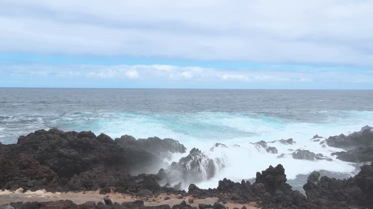 olas del océano chocando violentamente contra las rocas negras de la orilla, formación de espuma blanca, cielo azul, poder de la naturaleza