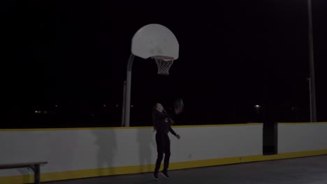 girl runs and does a layup in an outdoor basketball court at night with lights